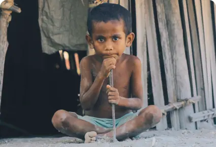 A child sitting in the doorway of a wooden house