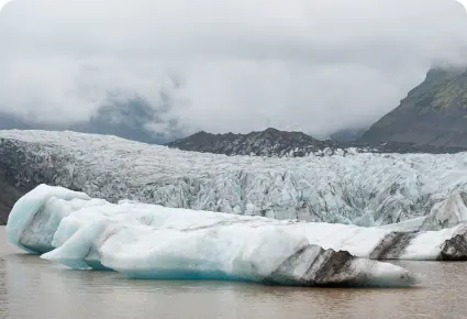 A glacier meeting a grey lake beneath a mountain
